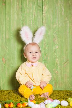 Little boy as a Easter rabbit on the grass with colorful eggs