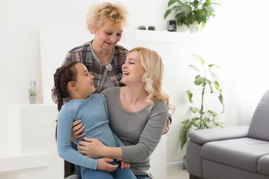 Portrait of three generations of women look at camera posing for family picture, cute little girl hug mom and granny enjoy time at home, smiling mother, daughter and grandmother spend weekend together