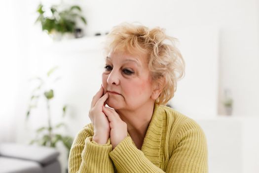 Attractive elderly woman sitting on couch at home, looking at camera, makes video call, communication distantly, modern wireless technologies concept