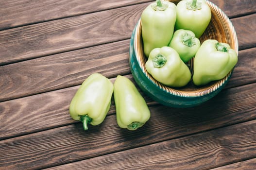 Fresh green peppers in bowl on wooden background.