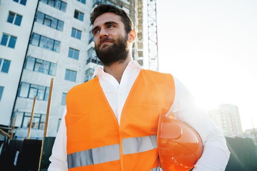 Builder wearing hardhat and safety vest standing on a commercial construction site, close up portrait