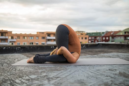 Woman enjoys  practicing yoga on the roof,Karnapidasana/Knee To Ear Pose.