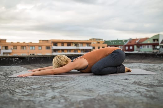 Woman  enjoys practicing yoga on the roof,Shashankasana/Hare pose.