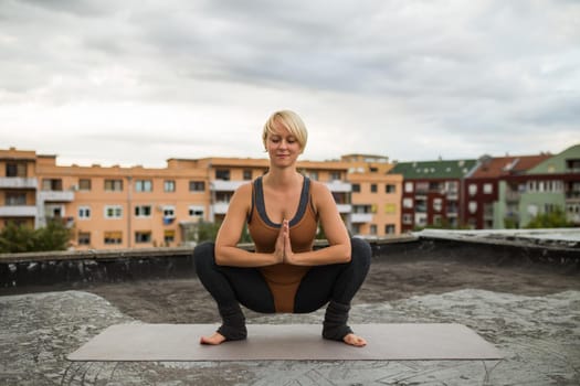Woman enjoys practicing yoga on the roof, Utkatasana/Buddhist stupa pose