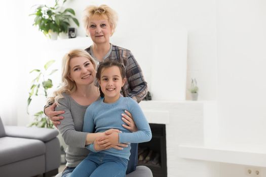 Portrait of three generations of women look at camera posing for family picture, cute little girl hug mom and granny enjoy time at home, smiling mother, daughter and grandmother spend weekend together