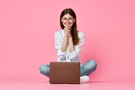 cheerful woman with laptop sitting on the floor on a pink background. High quality photo