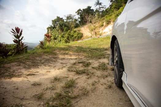 fender of a white car and wheel on the side of a cliff in the tropics close up