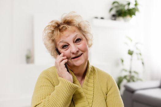 Concept of easy, fast usage of modern technology among all ages. Portrait of confident mature woman with wrinkles she is using her modern smartphone for sending a message isolated on gray background
