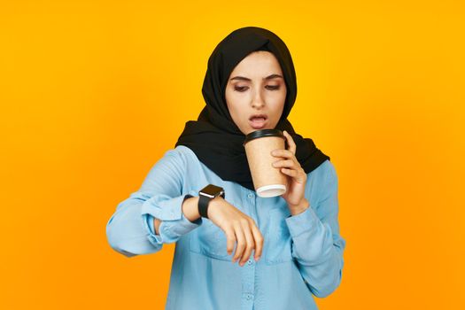 woman in black hijab with clock in hands technology emotions yellow background. High quality photo