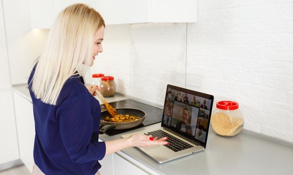 Beautiful girl is learning to cook healthy food online by the internet from a laptop in gray kitchen on table.