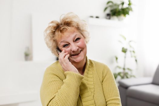 Happy senior woman talking on smartphone at home.