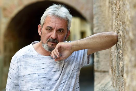 Portrait of a mature man looking at camera in urban background. Senior male with white hair and beard wearing casual clothes.