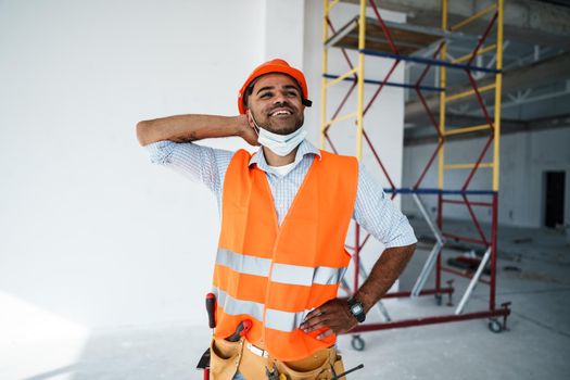 Portrait of mixed race man builder in workwear and hardhat wearing medical mask, close up photo