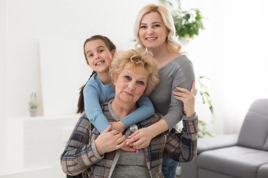 Portrait of three generations of women look at camera posing for family picture, cute little girl hug mom and granny enjoy time at home, smiling mother, daughter and grandmother spend weekend together