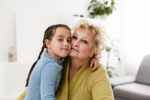 Senior woman hugging granddaughter while sitting on sofa at home
