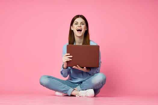 woman sitting on floor with laptop shopping entertainment pink background. High quality photo