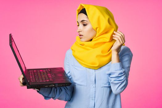 muslim woman in yellow hijab with laptop technology student pink background. High quality photo