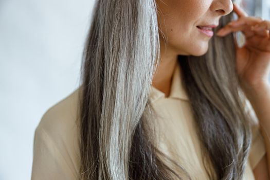 Middle aged woman with beautiful grey hair poses on light grey background in studio closeup. Mature beauty lifestyle