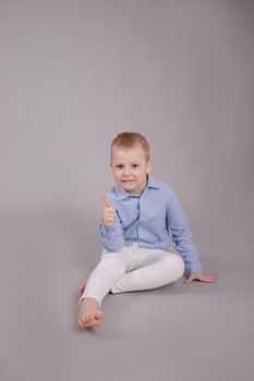 charming little preschool boy in white pants and blue shirt on gray background. child, kid.