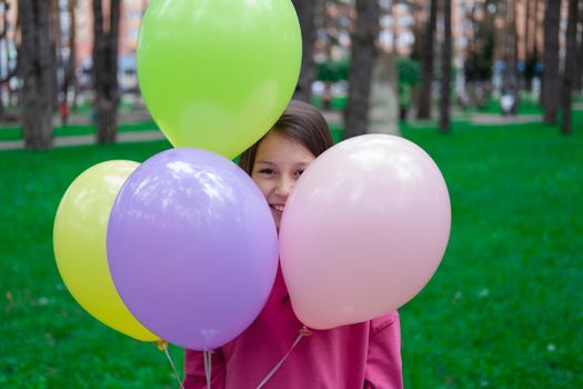 pretty tween teenager brunette girl in pink holding colorful hot air balloons outdoors. party, birthday concept. summertime. happy children. hollidays, summer break.