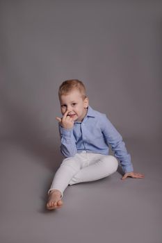 preschool blonde boy in white pants and blue shirt on grey background. child, kid isolated.