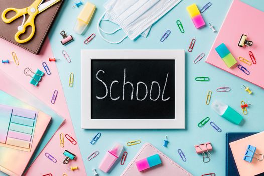 Blackboard with letters school made with chalk. School supplies, pencils, scissors and colored books on blue and pink background. Top view or flat lay. Back to school concept