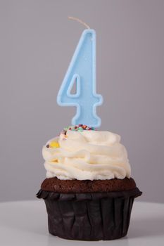 tasty chocolate cupcake with white topping cream and candle in shape of number four 4. on a white stand on a gray background. sweets, bakery. party food. dessert.