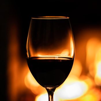 A wineglass of red wine on the background of the fireplace lights. Christmas holiday concept