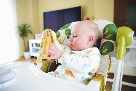 baby sitting in his chair eating banana.