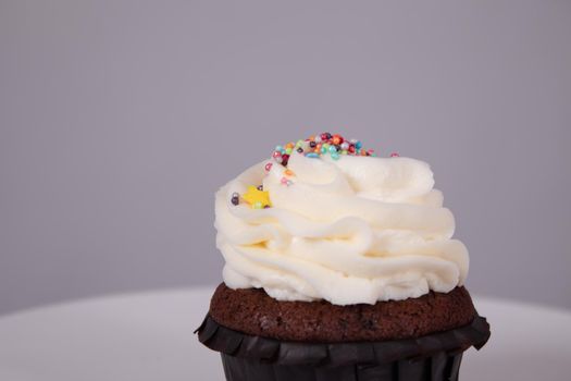 tasty chocolate cupcake with white topping cream on a white stand on a gray background. sweets, bakery. party food. dessert.