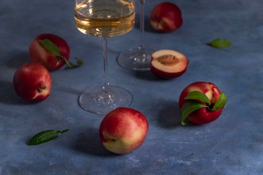 Several ripe peaches or nectarines and a glass of white peach wine sit on a blue plaster-textured surface. Wine drinking. Selective focus.