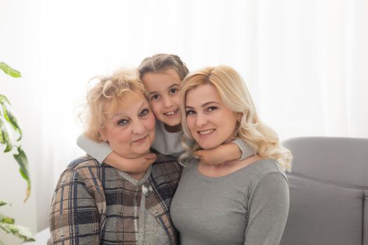 Portrait of three generations of women look at camera posing for family picture, cute little girl hug mom and granny enjoy time at home, smiling mother, daughter and grandmother spend weekend together