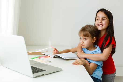 Two girls, the oldest and the youngest, are engaged at a table on a laptop.