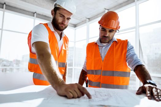 Two young engineers man looking at project plan on the table in construction site