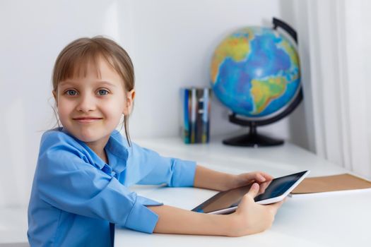 Cute little girl is sitting at table with her laptop and studying online