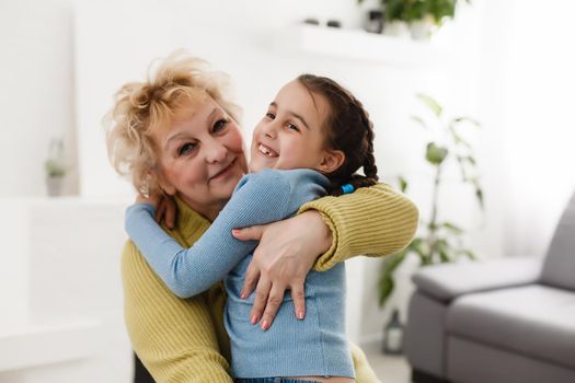 Little granddaughter and happy grandmother giving high five having fun playing together sitting on sofa, smiling grandma granny and preschool grandchild laughing celebrating good relations at home