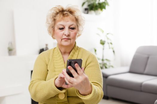 Upset elderly woman using touch screen mobile for taking selfie or making video call