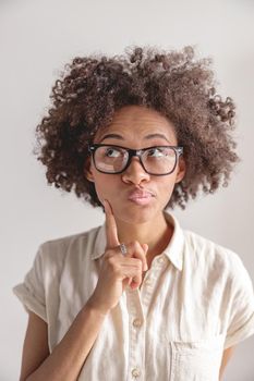 Portrait of thoughtful Afro American woman holding a finger near the cheek and looking up, isolated on grey background