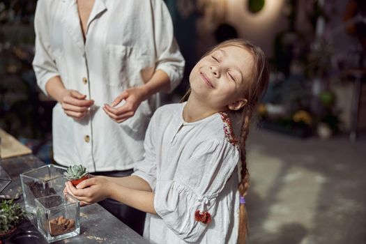 caucasian confident happy florist is working with her young daughter and making composition from glass stones and plants in botanic shop