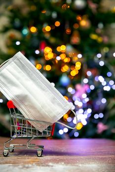 Protective safety mask in iron shopping basket near Christmas tree, Covid-19, coronavirus, holiday concept with copy space and bokeh lights background space for text