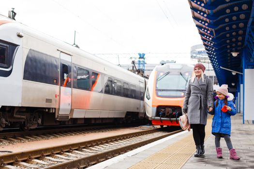 Yound woman and little girl, lovely daughter, on a railway station. Kid and woman waiting for train and happy about a journey. People, travel, family, lifestyle concept