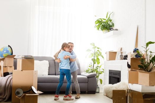 two little daughters celebrating moving day, excited by relocation into new house, laughing living room with cardboard boxes