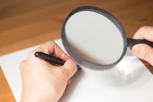 very aged person is writing on a paper with Magnifier