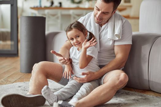 Full length portrait of happy daughter in dad arms sitting on floor while spending active time at home