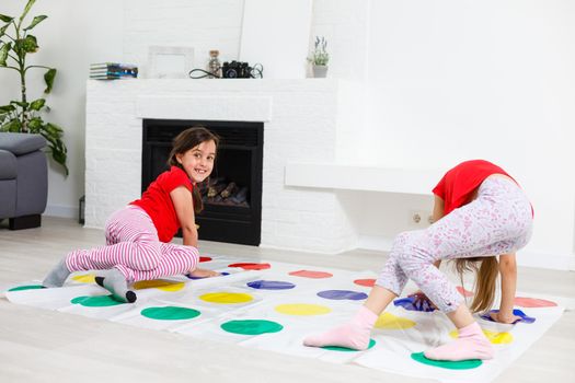 Two happy girls in children's clothes enthusiastically play on the floor.