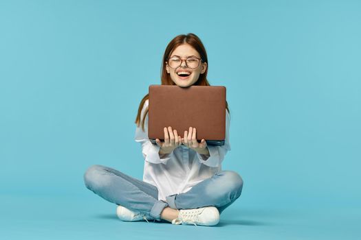 woman with laptop sitting on the floor learning student technology blue background. High quality photo