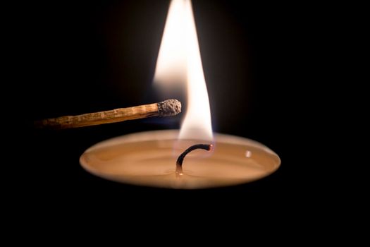 Candle ignited a match on black ground