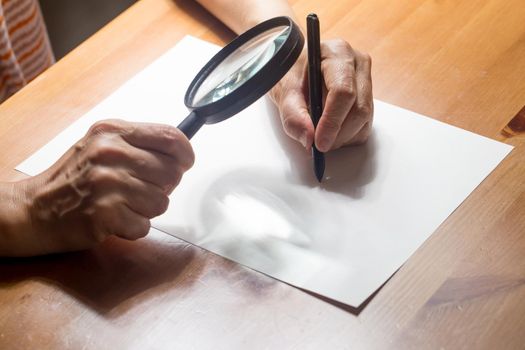 very aged person is writing on a paper with Magnifier