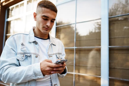 Young urban casual man using smart phone while walking in the street, close up