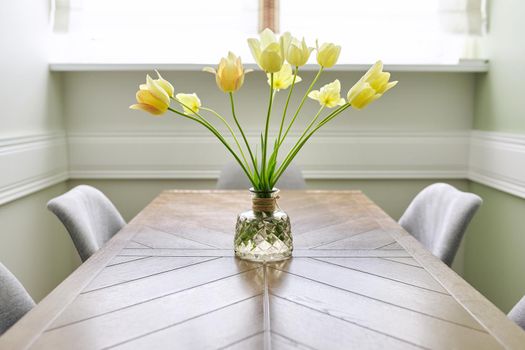Vase with a bouquet of yellow tulips on a wooden table in the interior of the living room